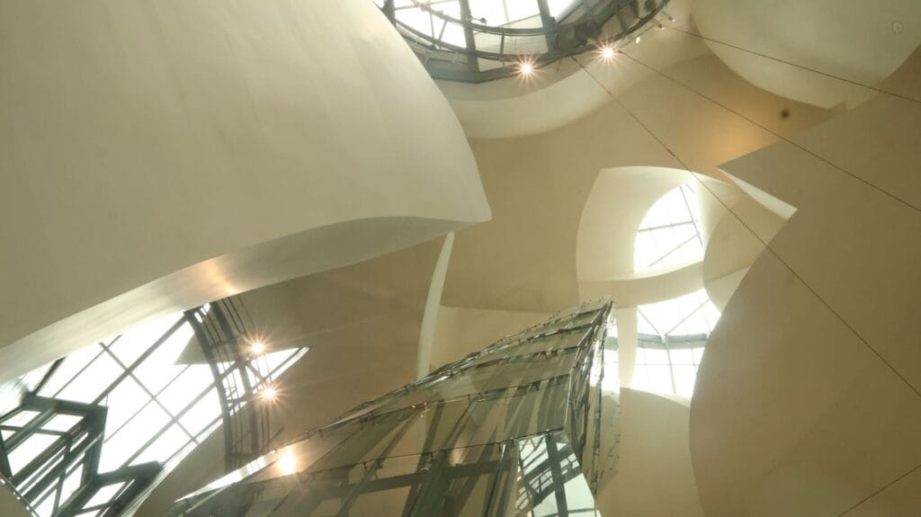 Strategische Transformatie - Interior of a modern white architectural atrium with curved walls and a glass staircase reaching upward toward skylights.